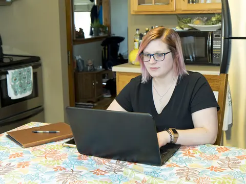 Female student with glasses using a laptop at a kitchen table.
