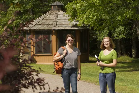 two girls standing outside with books, bags, and sunglasses