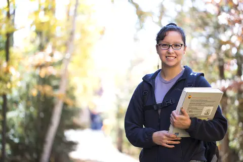 Female student holding books on path going to class
