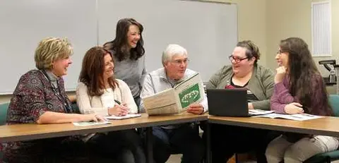 Group of six adults smiling around a table in a classroom setting.