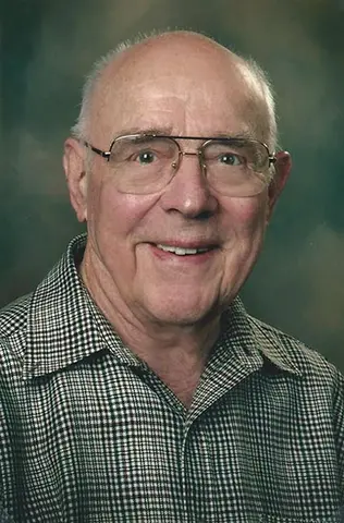 Tug Juday: Elderly man with glasses smiling in a plaid shirt.