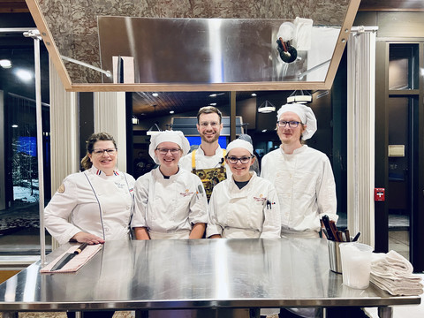 group of student chefs and instructors standing behind a prep table