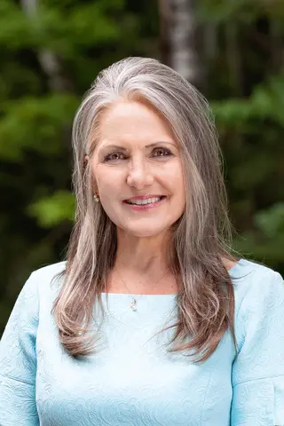 Woman with long gray hair, smiling outdoors.