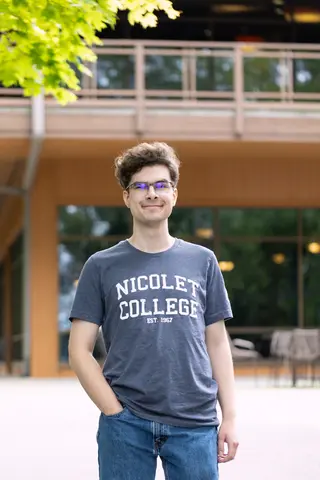 Male student standing outside in Nicolet College t-shirt and jeans