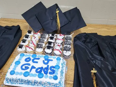 Graduation caps, gowns, cupcakes and cake displayed on a table.