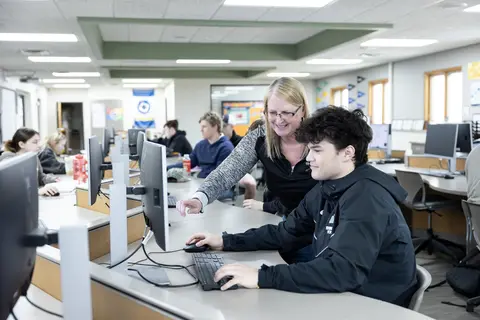 A high school teacher and students in a classroom with computers.