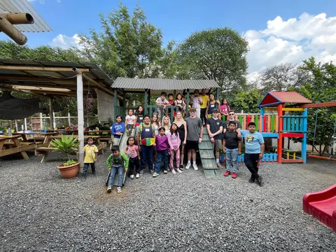 Group of people smiling in a playground with colorful equipment and trees.
