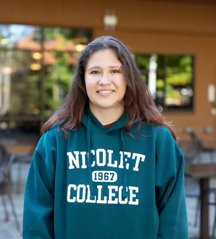 Young woman in a green Nicolet College hoodie, smiling outdoors.