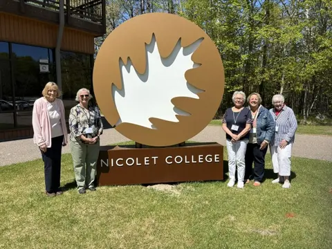 Group of five people standing by a large leaf-shaped sign for Nicolet College.