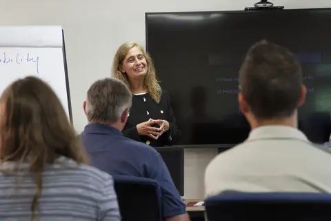 Female facilitator in front of a room of several adults