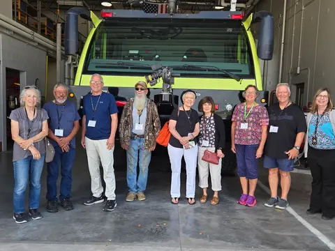 Group of senior citizens posing in a line in front of a large airport truck.