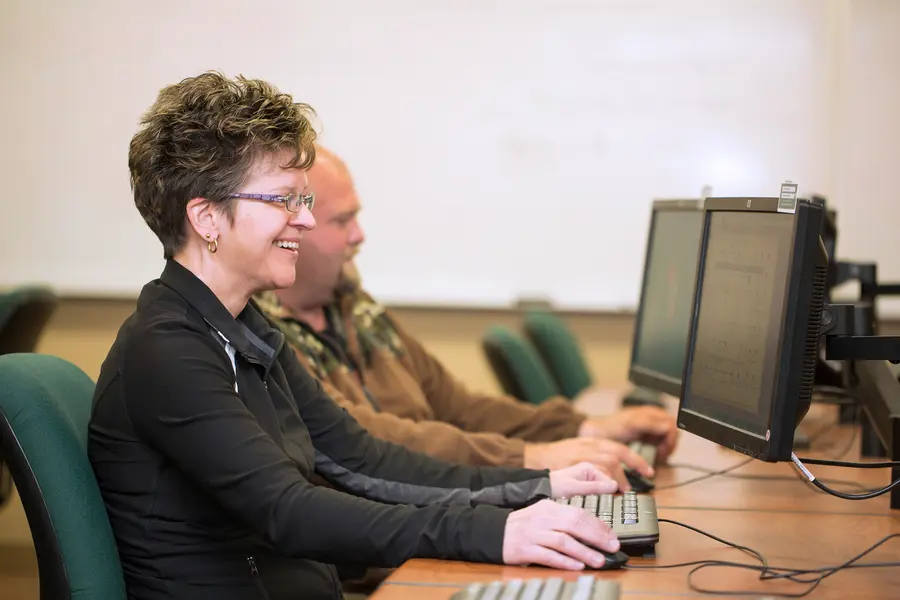 Two people smiling while working on computers in accounting class.
