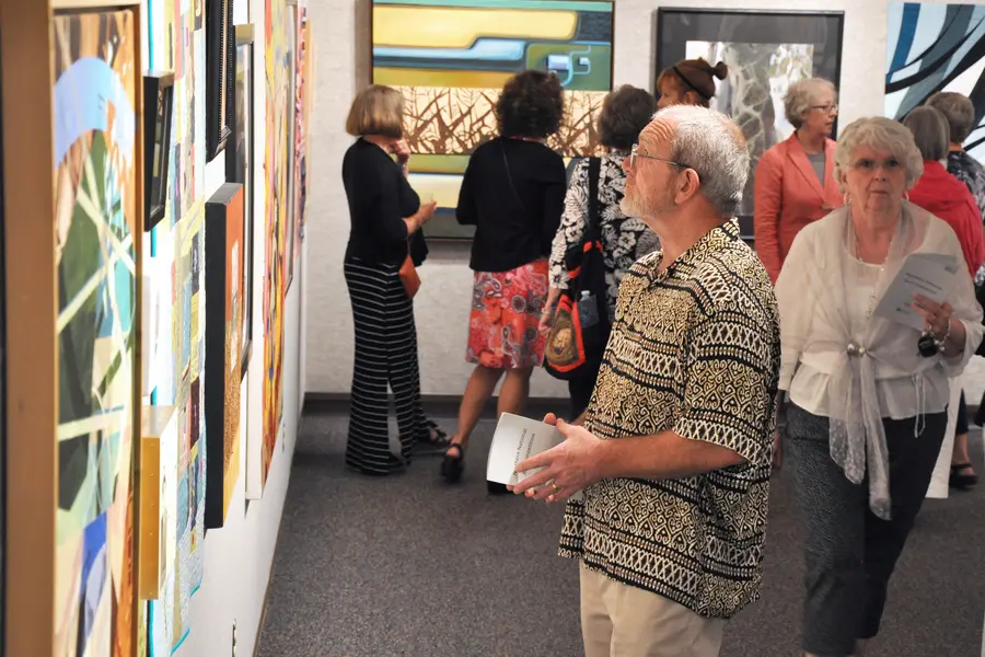 Art gallery with people viewing colorful paintings on the walls.