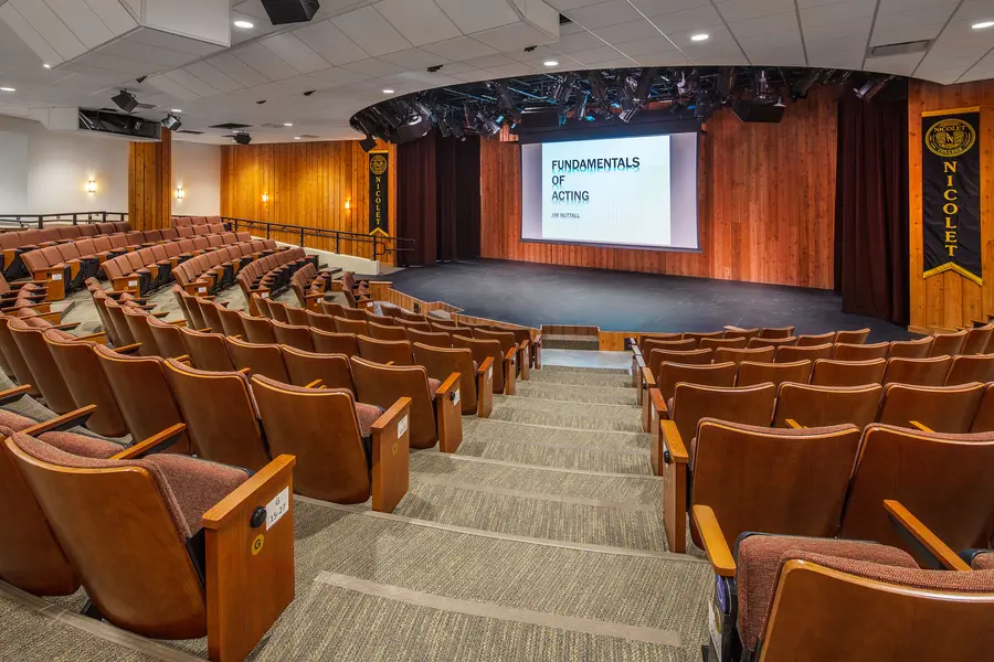 Theatre with rows of brown seats facing a stage and projector screen reading "Fundamentals of Acting."