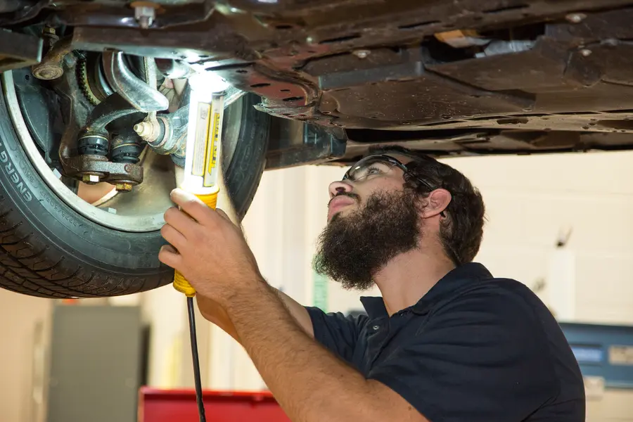 Automotive student looking under car with flashlight.