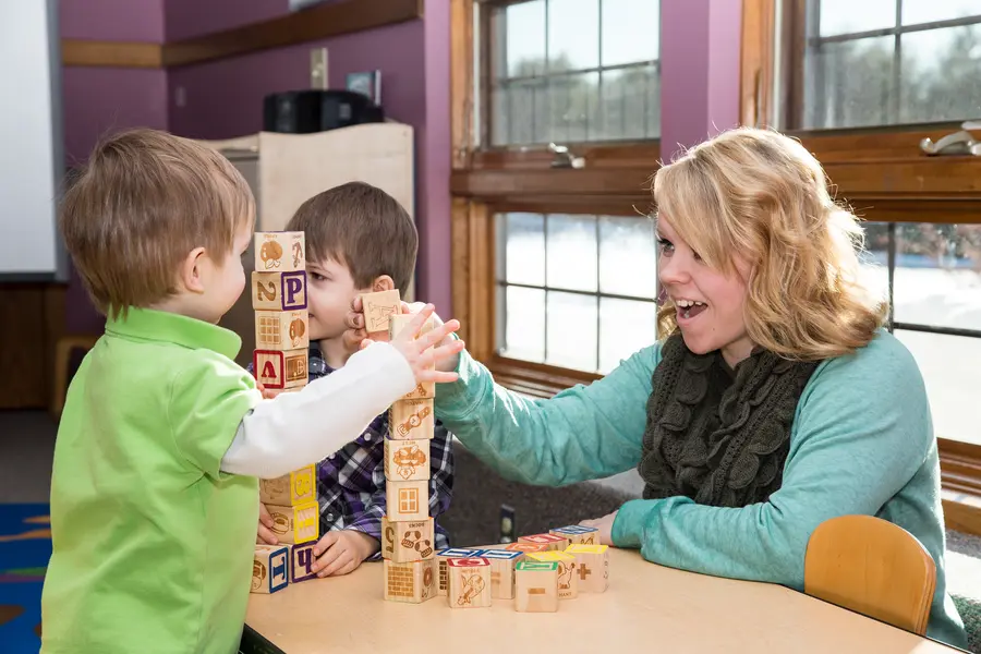 Female early childhood education student and two children playing with wooden building blocks.