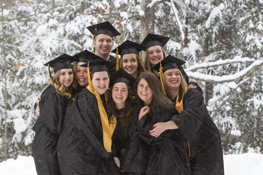 Graduates in caps and gowns smiling in snowy forest setting.