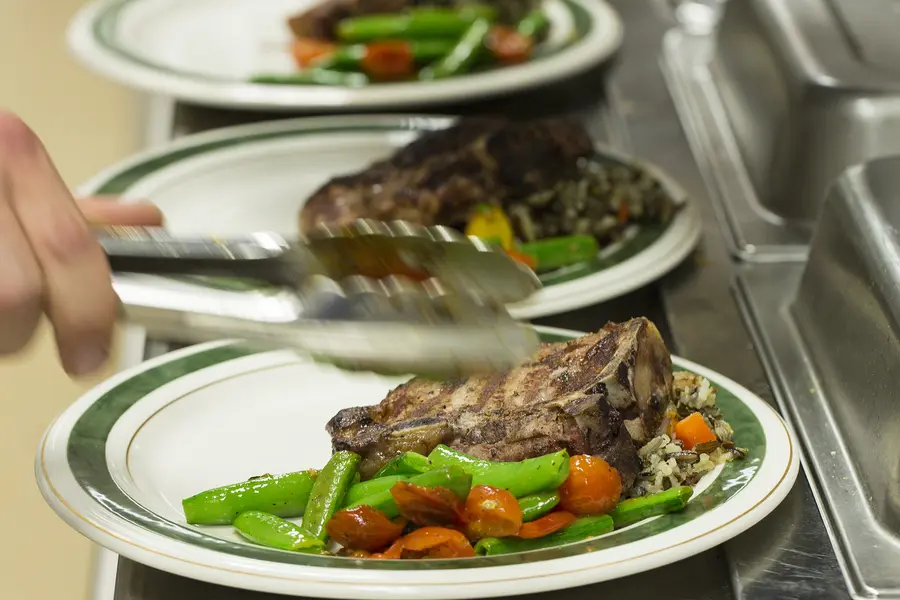 Steak dishes being garnished with vegetables in a restaurant kitchen. 