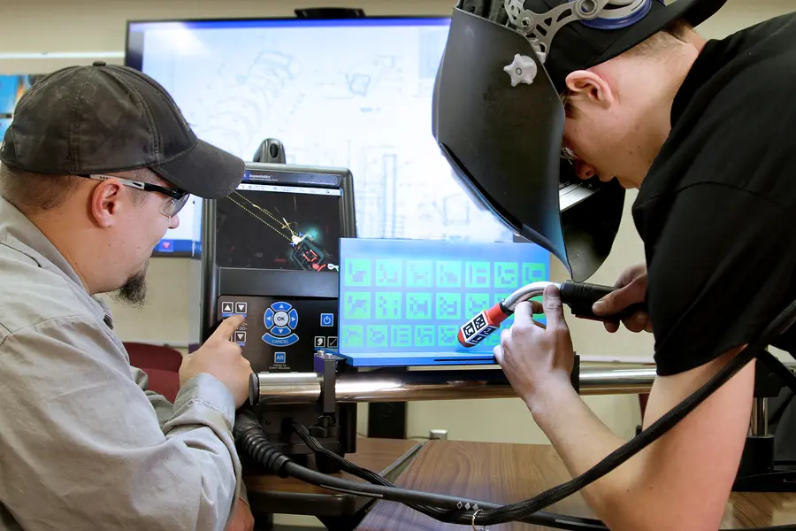 Two people using welding simulators with a digital screen display.