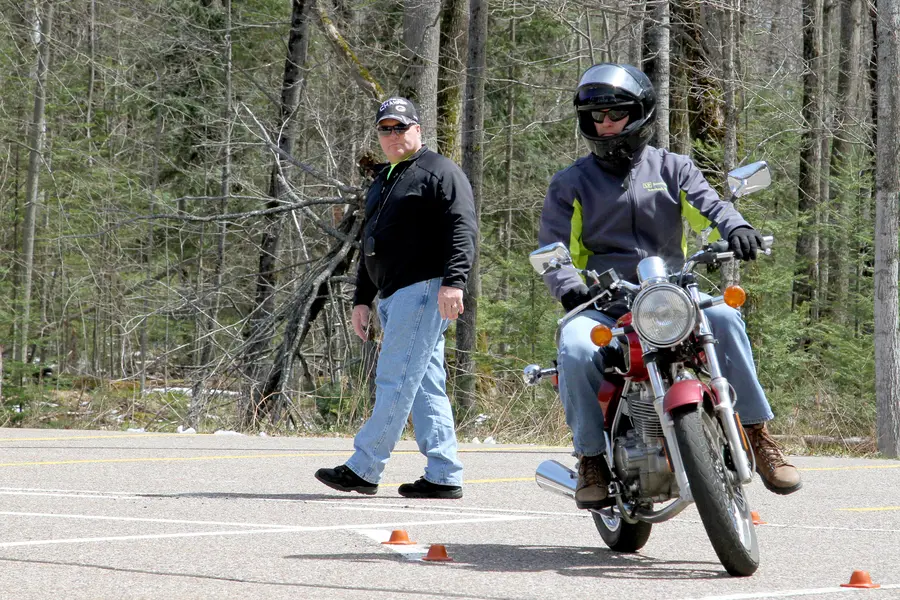 Motorcyclist practices in parking lot while instructor observes.