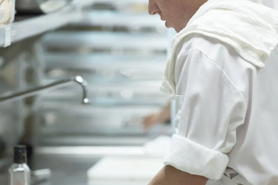 Culinary student in white uniform preparing food in a restaurant kitchen.