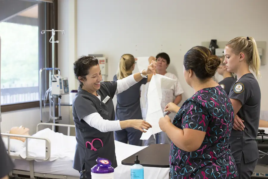 Nursing students practicing patient care and sanitary preparation in a hospital simulation room.