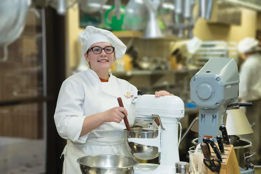 Culinary student in white uniform using a stand mixer.