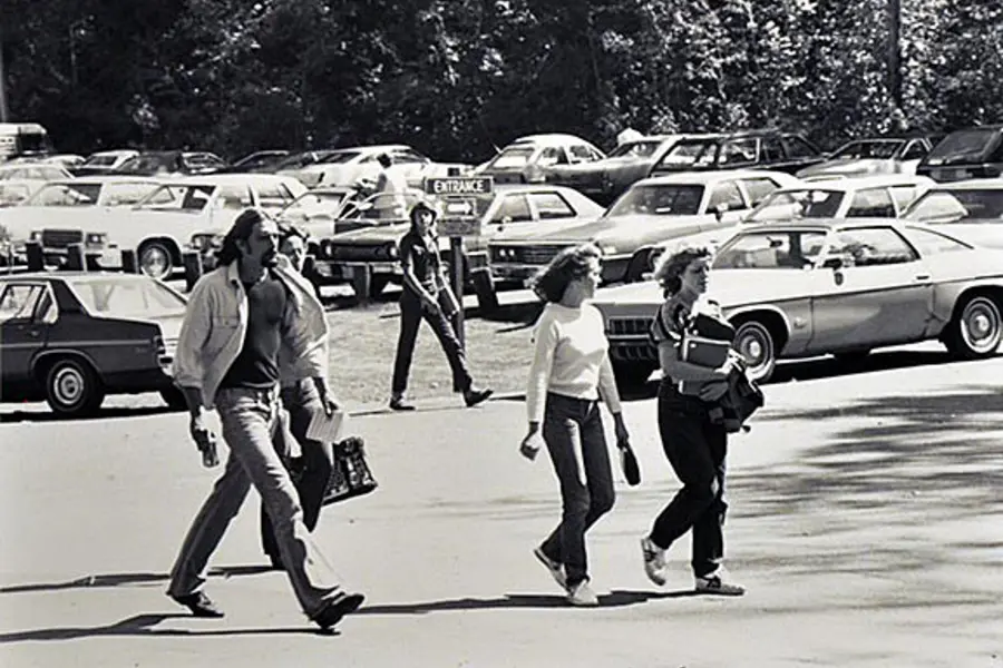 Students walking in campus parking lot with vintage cars in the background, black and white photo.