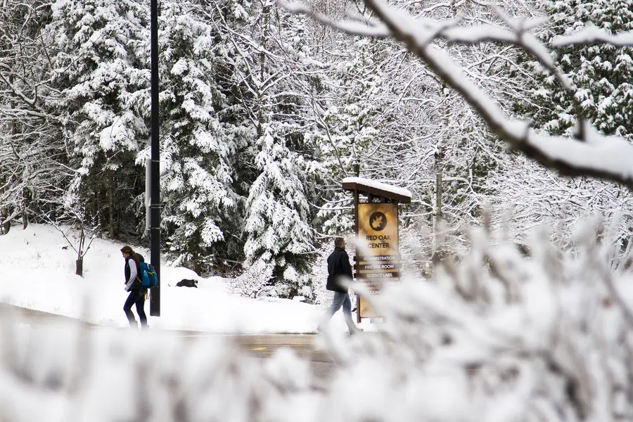 Two students walking on campus with snow covered trees and Red Oak Center sign in the background.