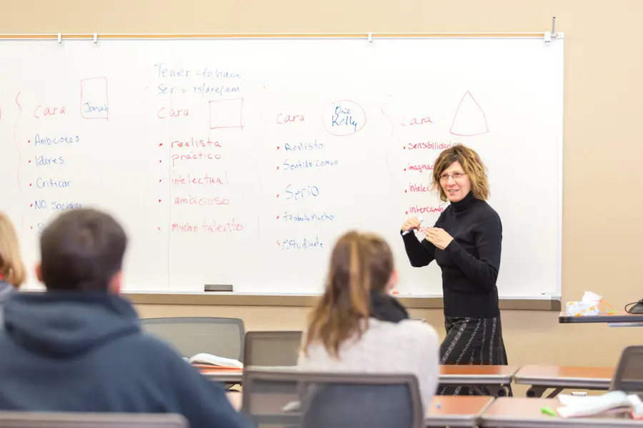 Spanish instructor at whiteboard speaking to attentive students in a classroom.