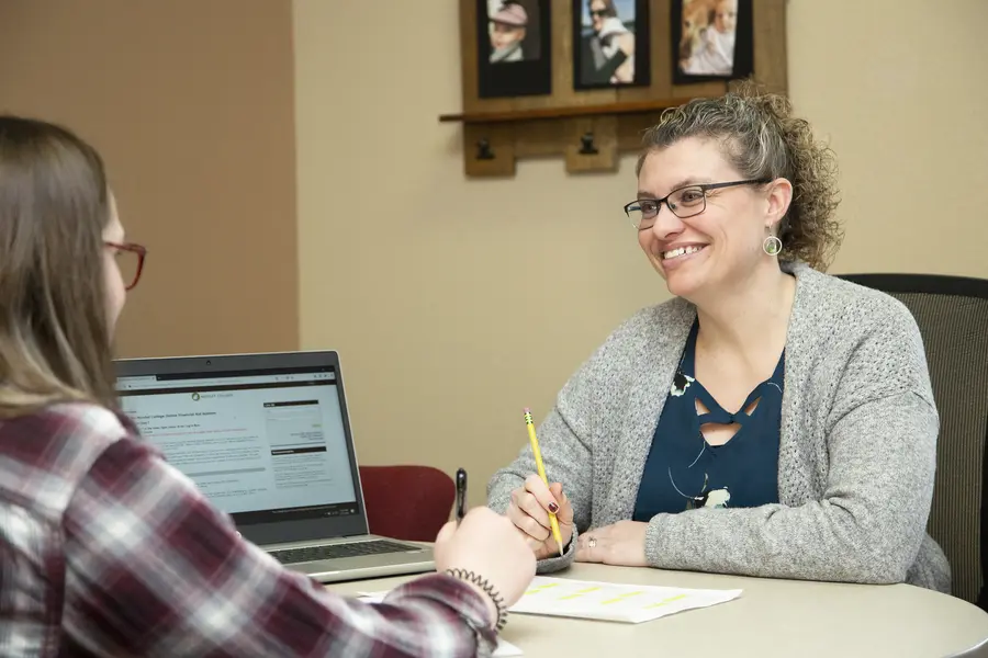 Financial Aid Advisor with student at a table, smiling and discussing.