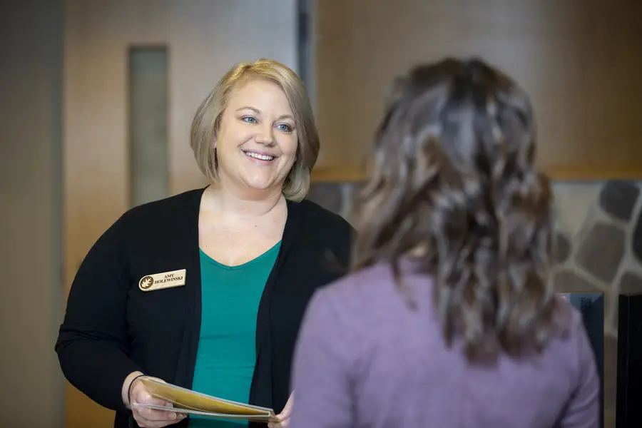 Smiling female Welcome Center employee holding papers, talking to a student.