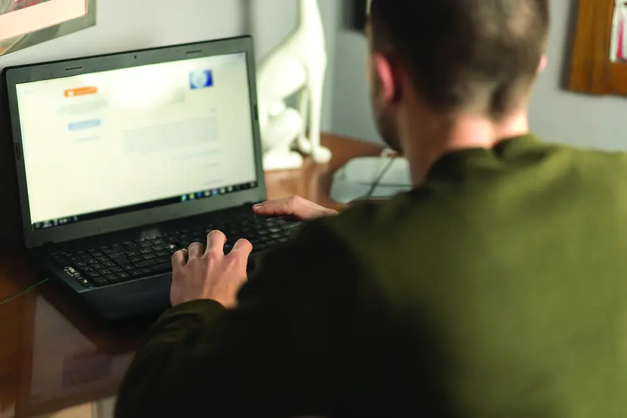 Male Web Developer typing on a laptop at a wooden desk.