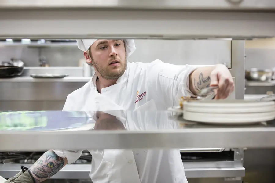 Culinary student plating food in a busy kitchen.