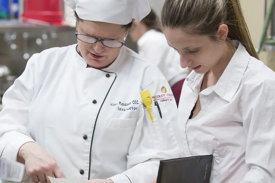 Culinary instructor conversing with culinary student in a kitchen.