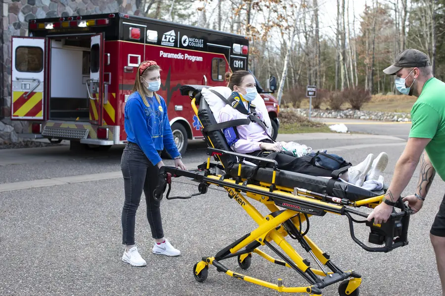 Two EMT students wheeling a patient on a stretcher to an ambulance.