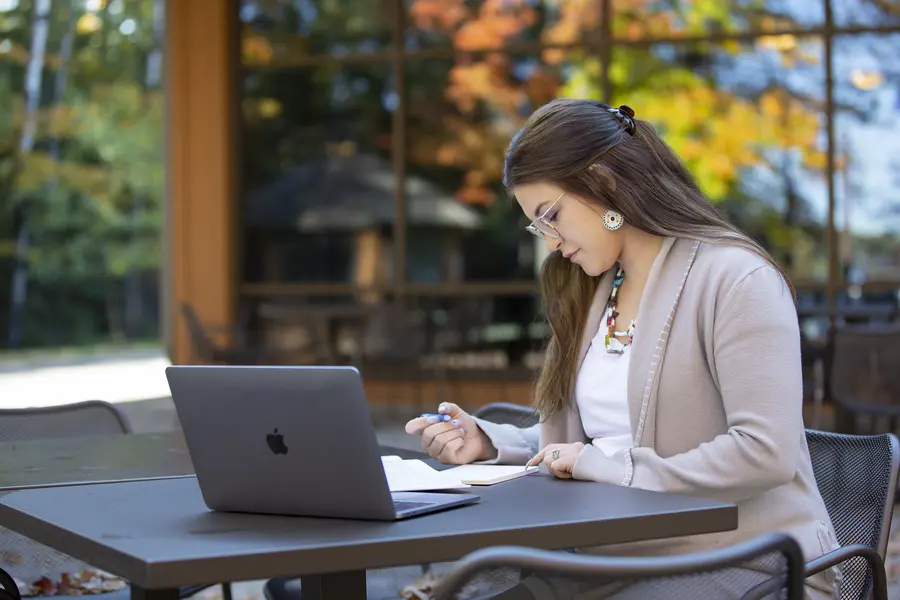 Female student working with a laptop and notepad outside the Lakeside Centerin autumn.