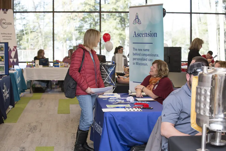 Job fair with people interacting at tables filled with informational materials.