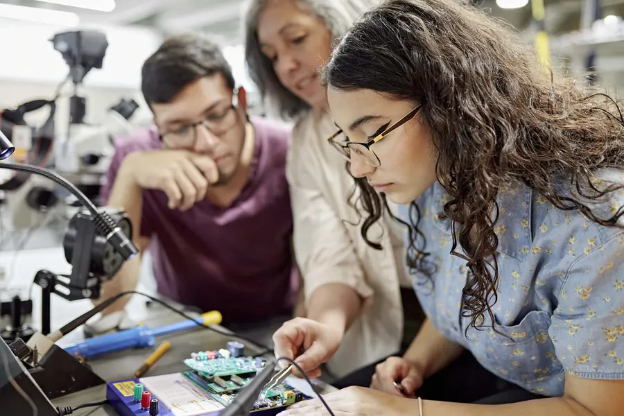 Two Engineering students and instructor working on electronics at a table, focused and collaborative.