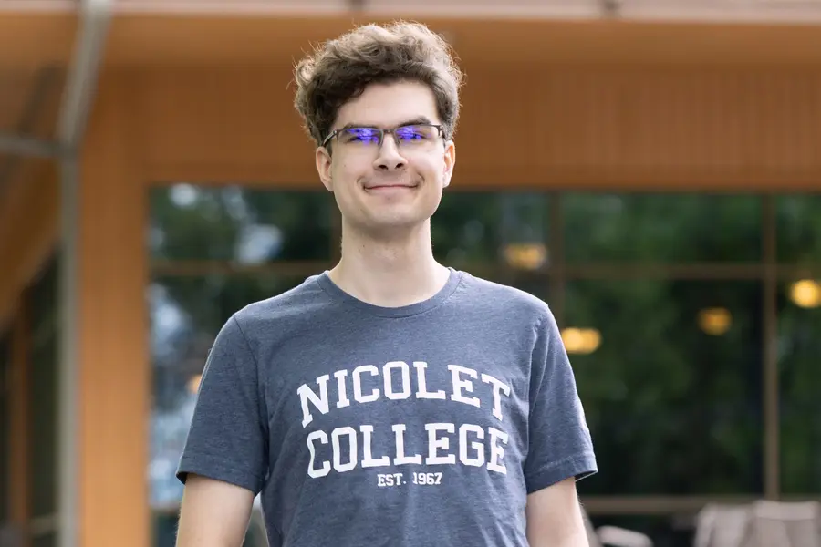 Male student standing outside in Nicolet College t-shirt and jeans
