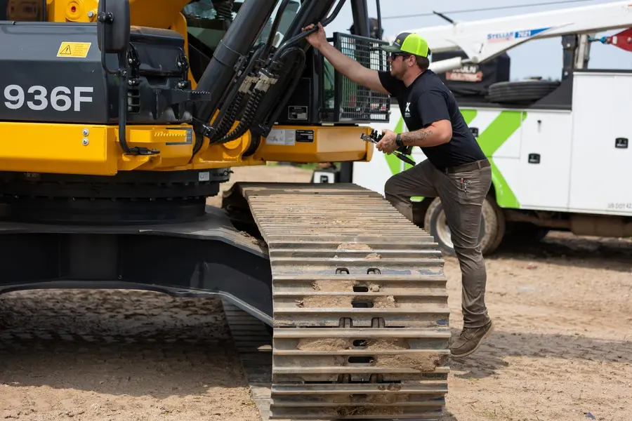 A field service technician climbing on an excavator to repair it.