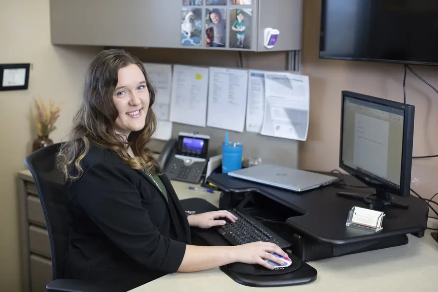 Woman smiling at a desk with a computer and office supplies.