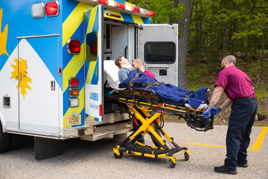 Paramedics loading a person on a stretcher into an ambulance.