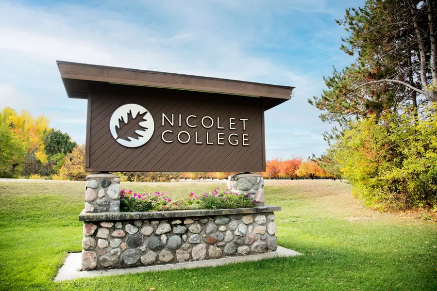 Nicolet College sign on stone base, surrounded by green grass and autumn trees.