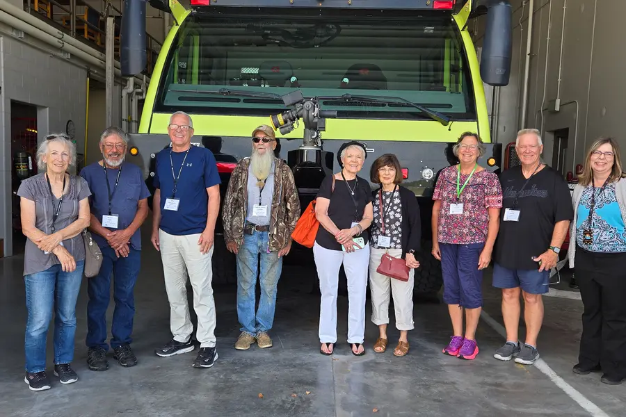 Group of senior citizens posing in a line in front of a large airport truck.