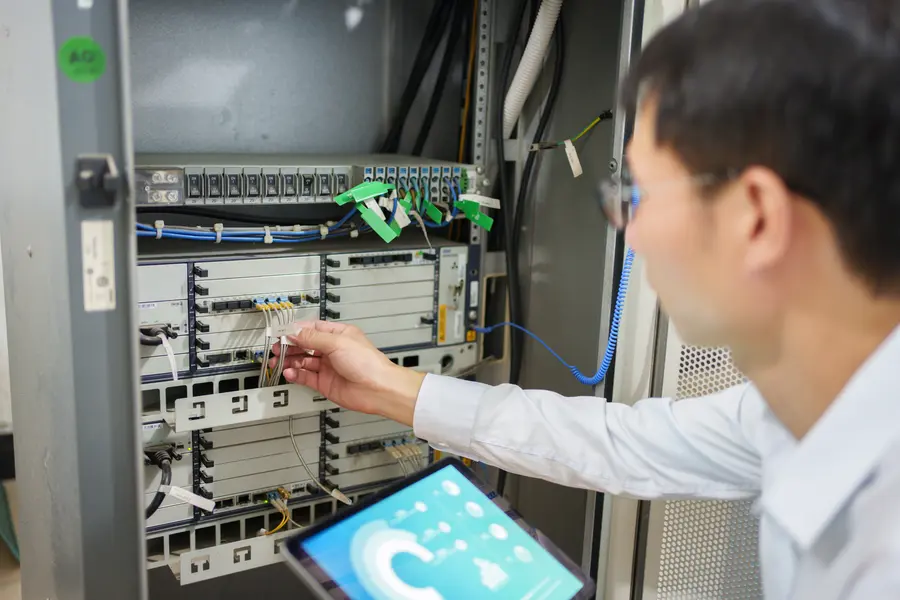 Technician working on a network server rack, holding a tablet.