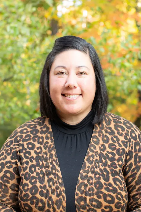 Smiling person in leopard print jacket, autumn leaves in background.