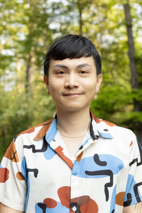 Smiling person in a colorful shirt with a blurred green forest background.
