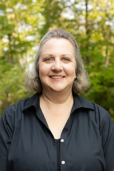 Smiling woman in a black shirt outdoors, with trees in the background.
