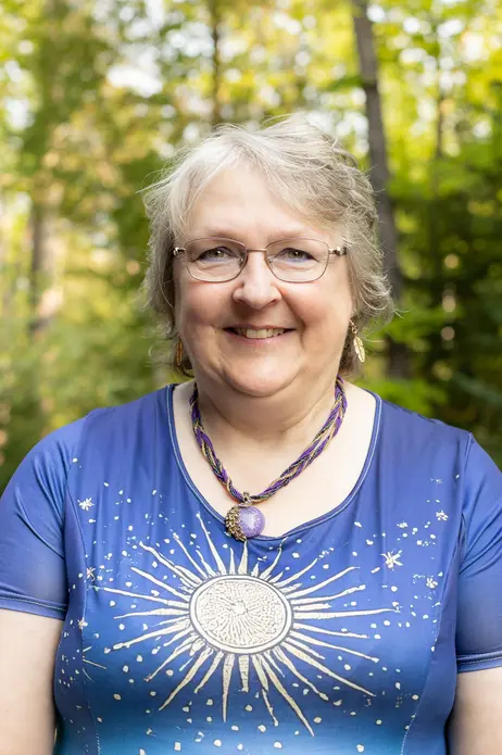 Smiling person in a blue shirt with sun design, green forest background.